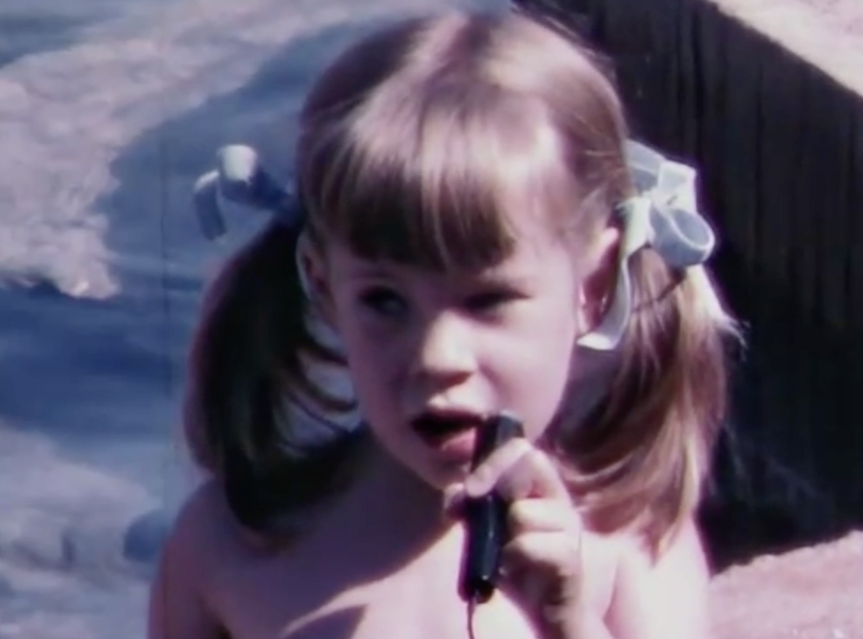 Anne Mühlethaler as a toddler holding a microphone with the sea in the background
