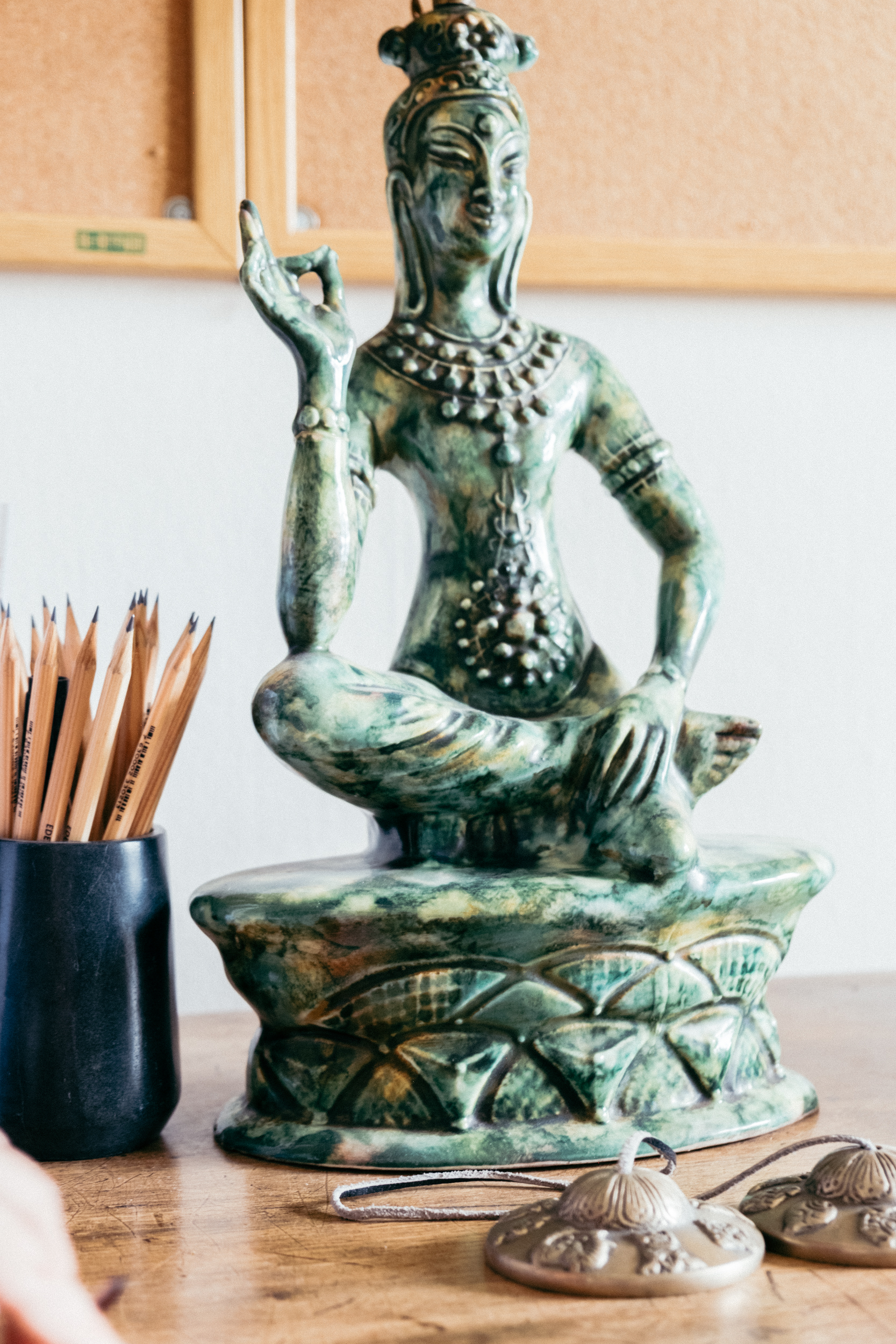 A close up of a vintage, green buddha ceramic lamp with Tibetan bells in front of it