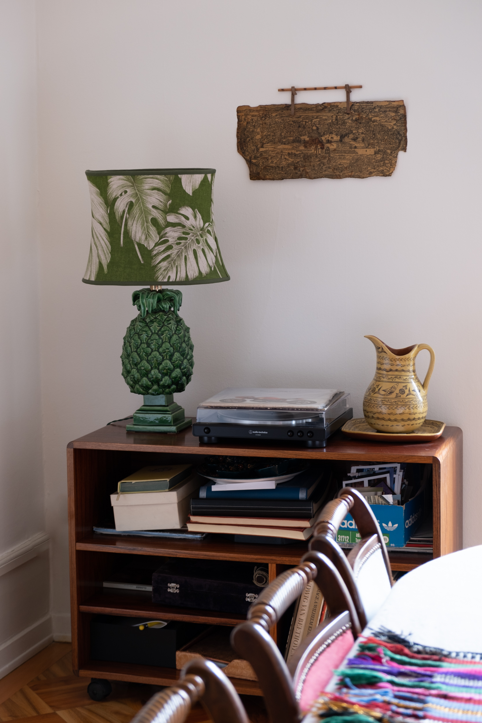 A picture of a side board in the dining room with a vintage pineapple lamp, a turntable and a yellow mexican ceramic jug