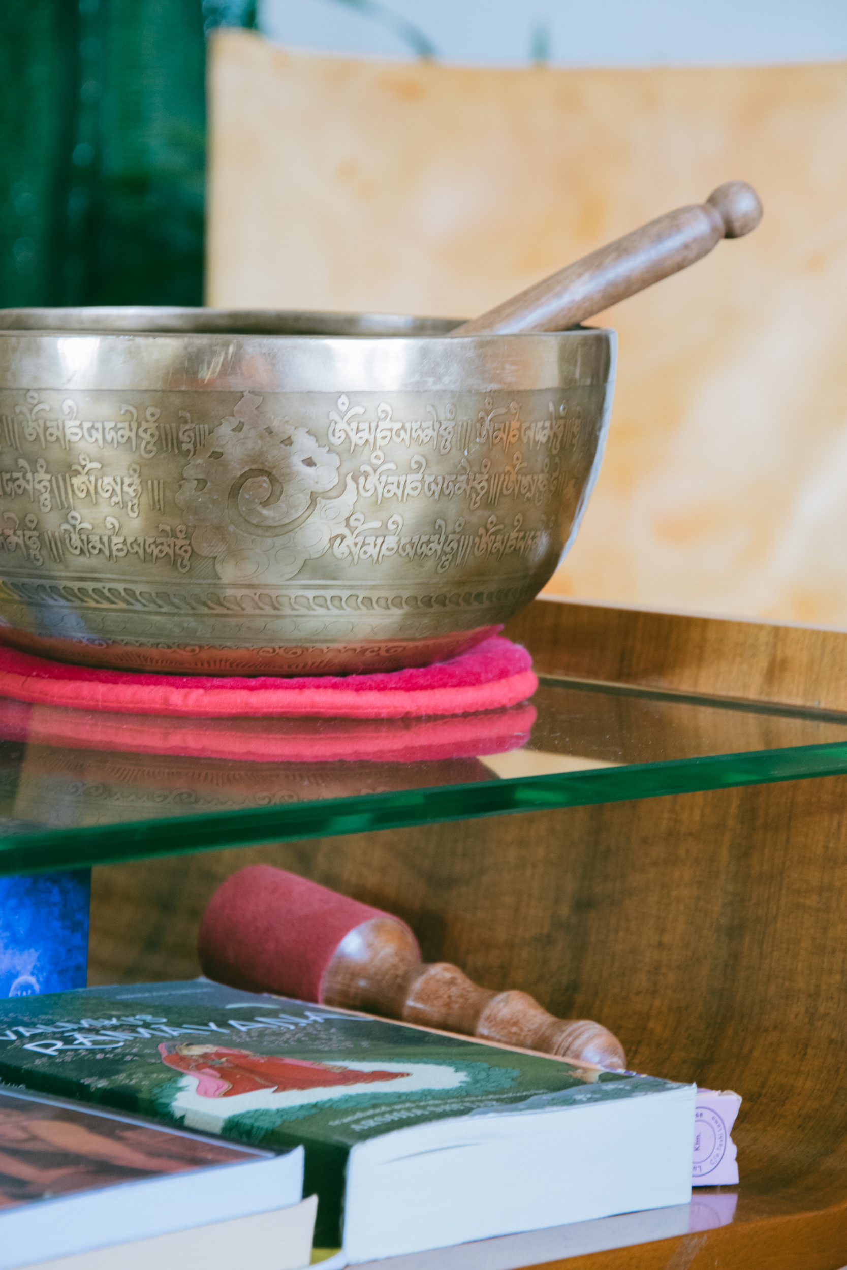 An up close shot of a Tibetan singing bowl, on a vintage glass and wood table, over a tome of the Ramayana
