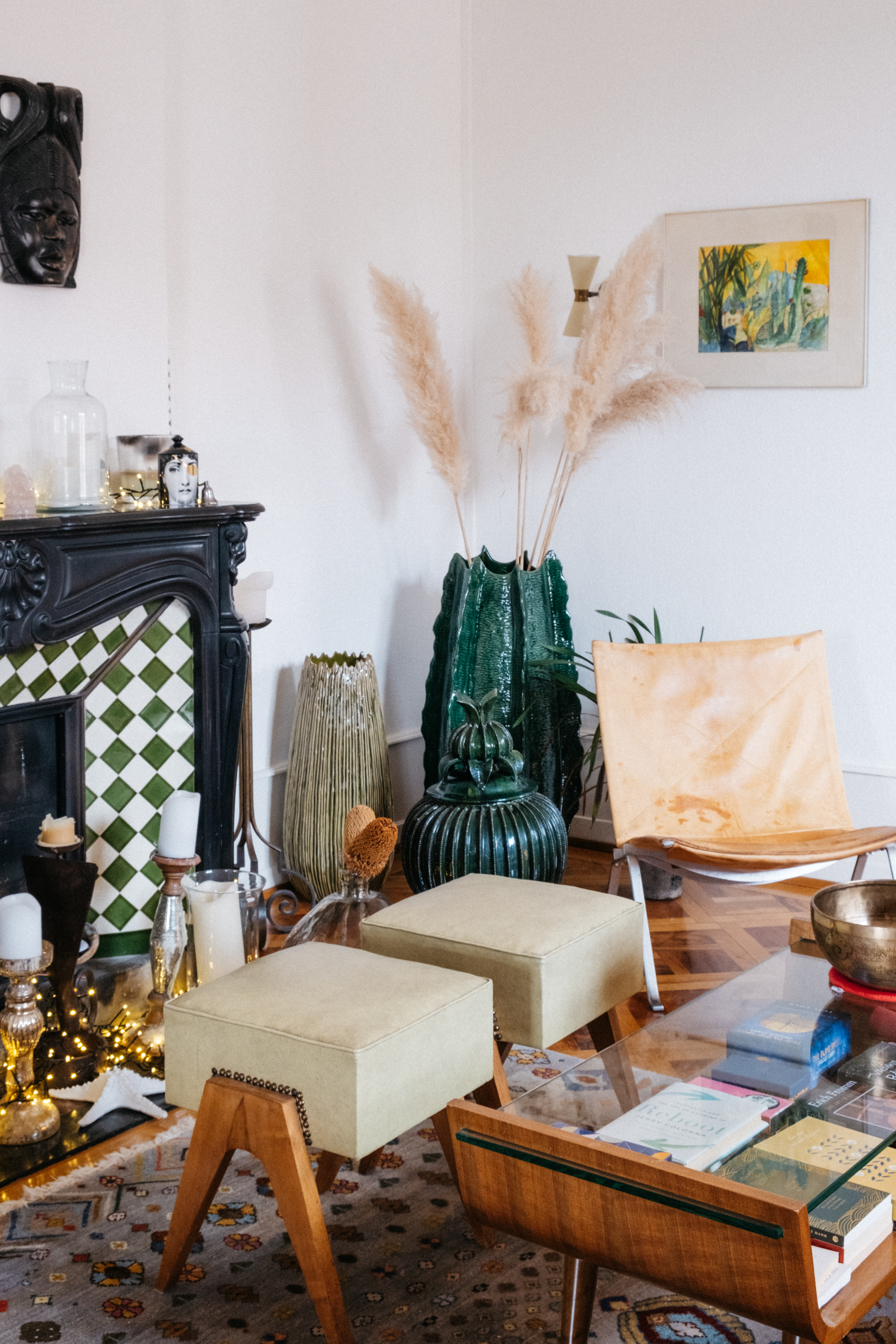 A photograph of the second living room including a beautiful green, white and black fireplace, green mexican ceramics next to a vintage beige leather chair with a framed painting on the wall