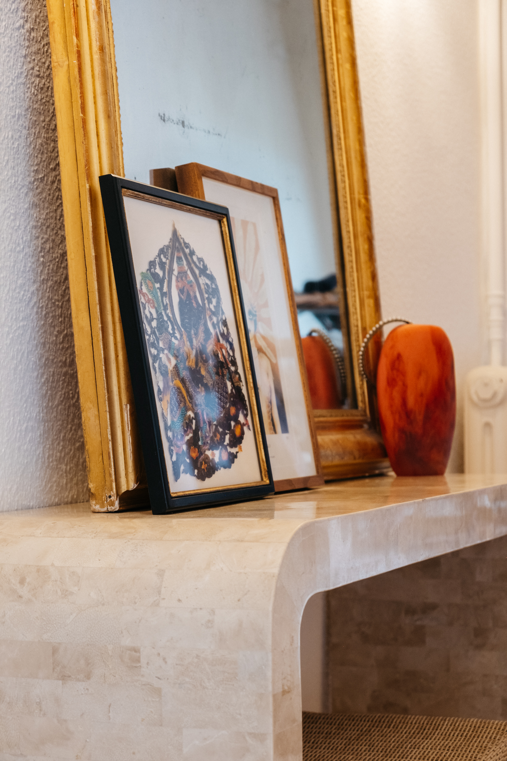A being marble console with a large vintage mirror decorated with a couple of framed art prints and a red marbled vase