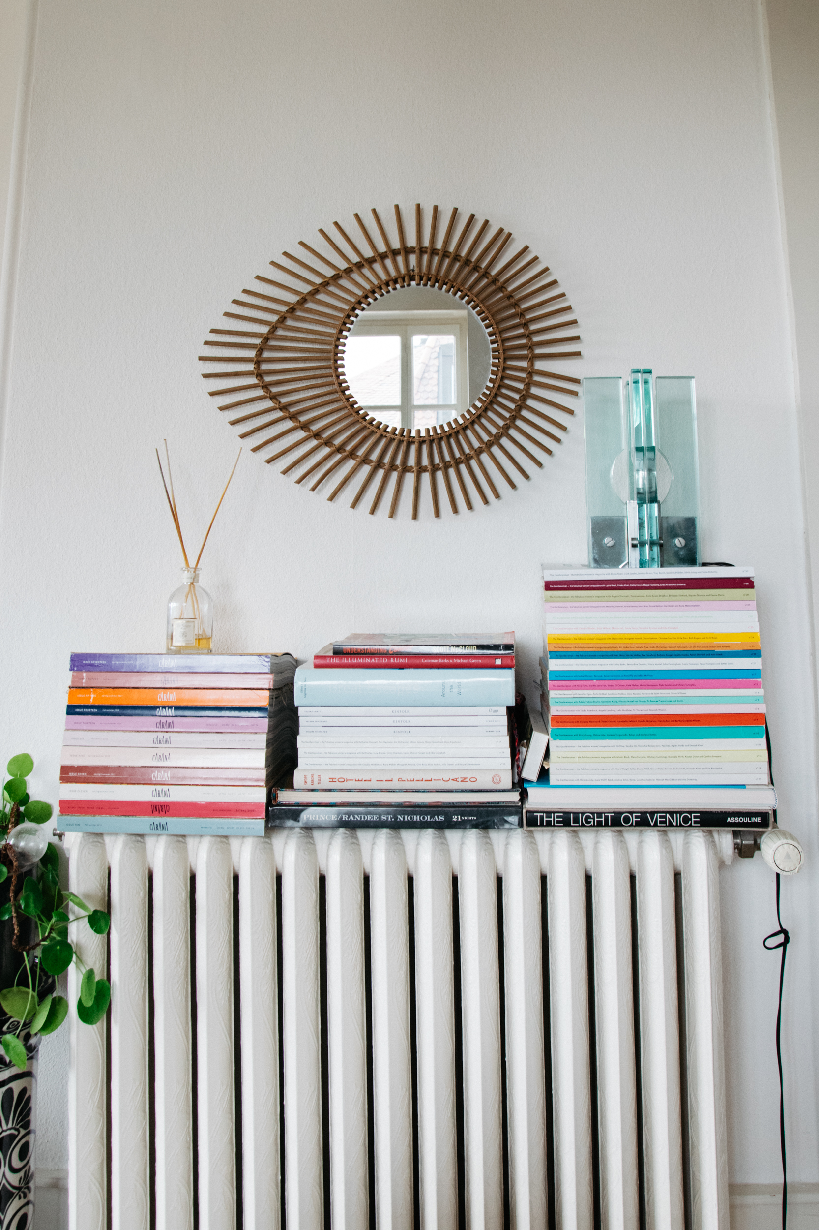 Magazines atop a vintage heater with an Italian vintage lamp and a sunburst mirror on the wall