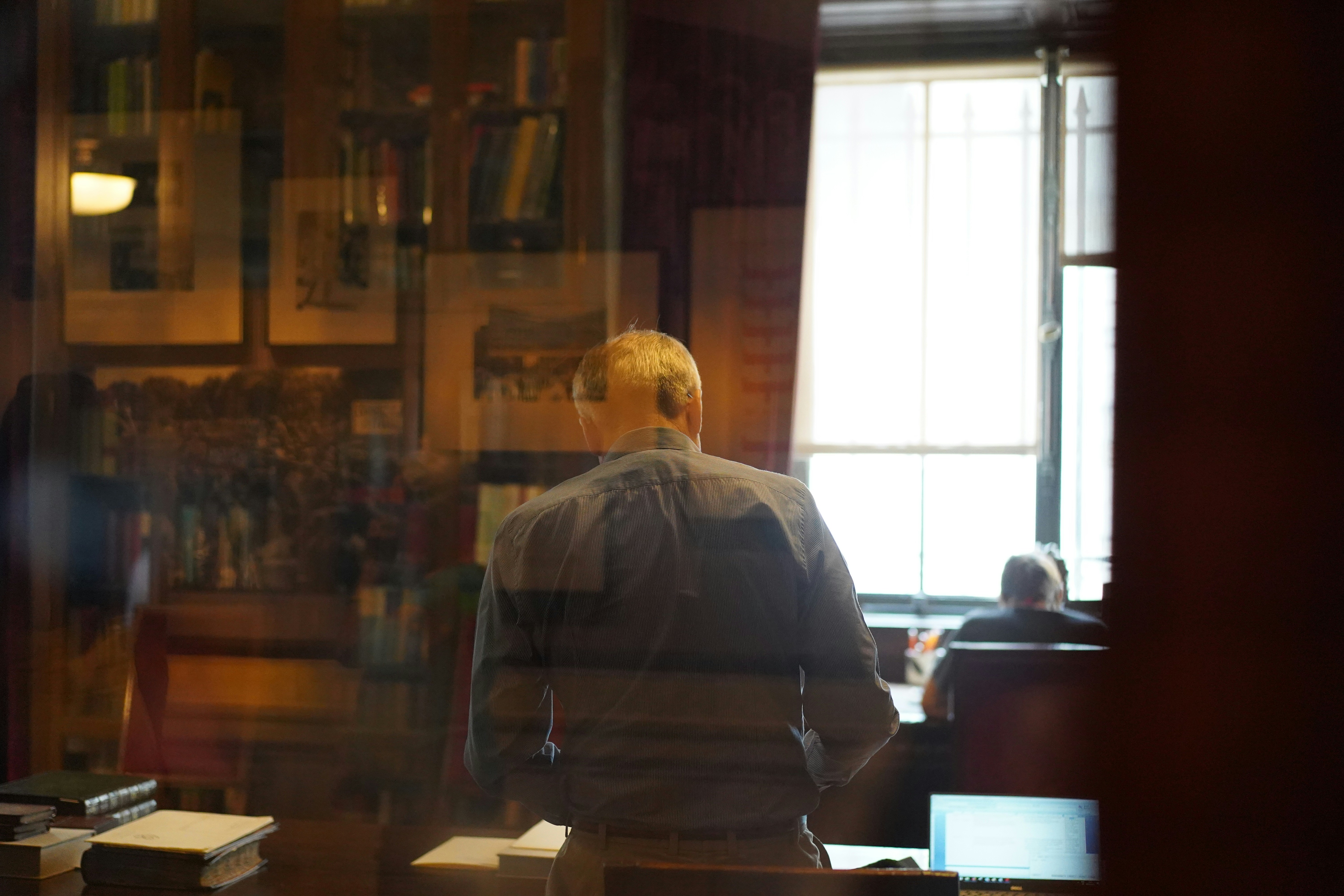  A picture of an older man near a desk and books, photographed from the back