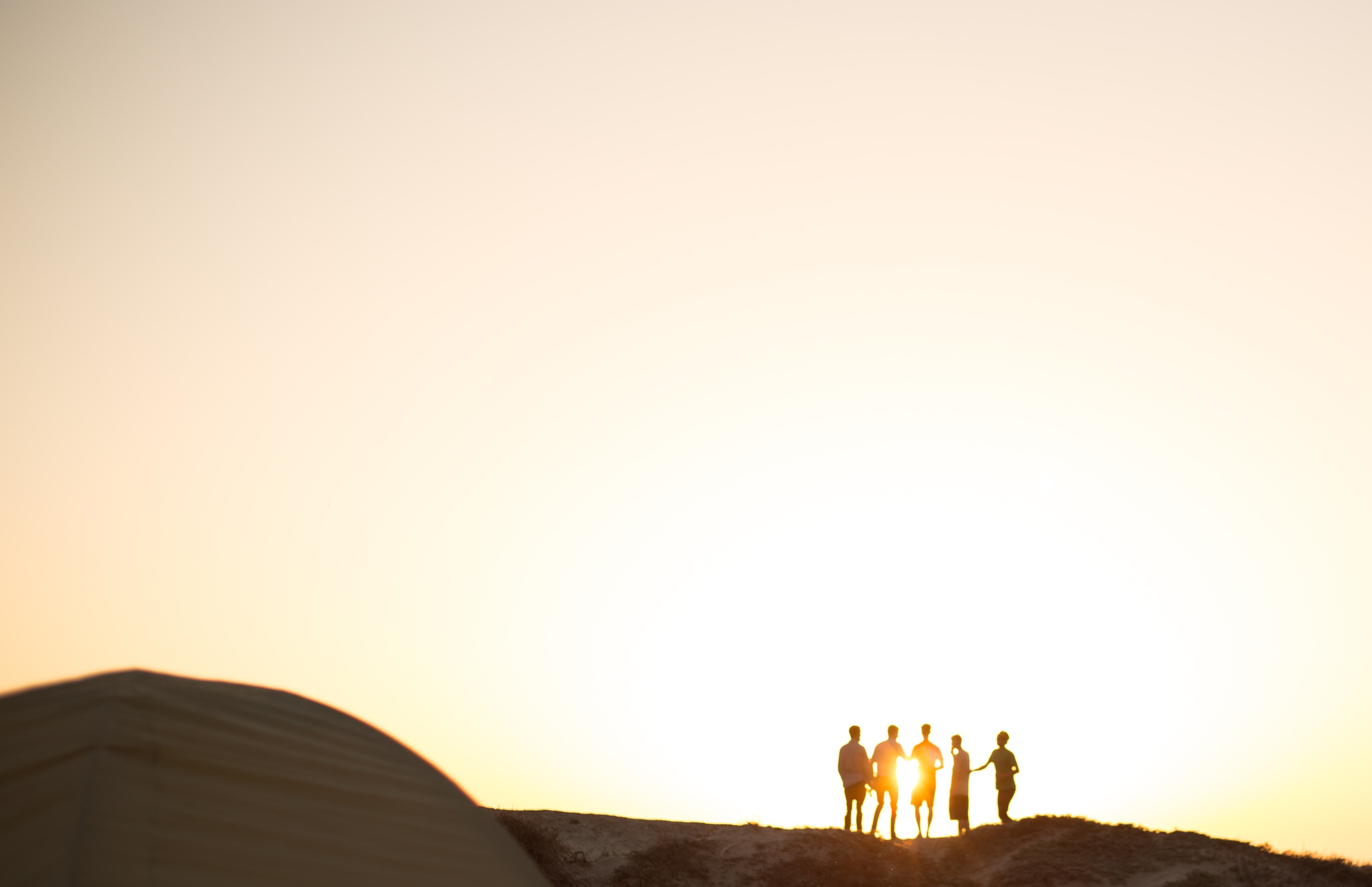 A picture on a mountain at sunset with the silouhette of a few friends leaning on each other 