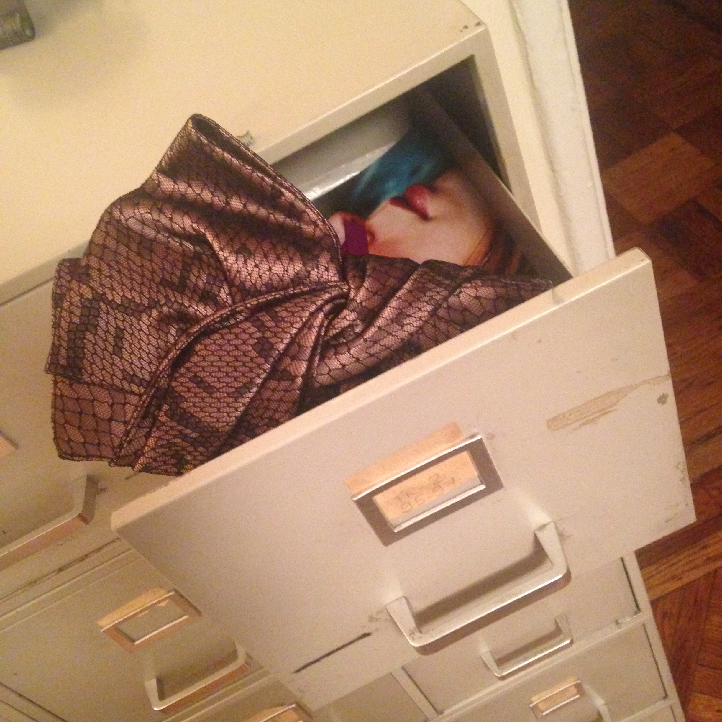 A picture of a Louboutin clutch bag in a metal drawer in front of a portrait of Anne Muhlethaler